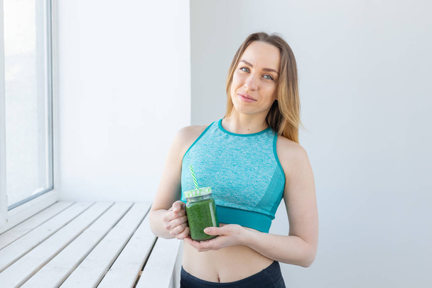 Healthy, diet, detox and weight loss concept - young woman in sportswear with green smoothie - Фото, зображення
