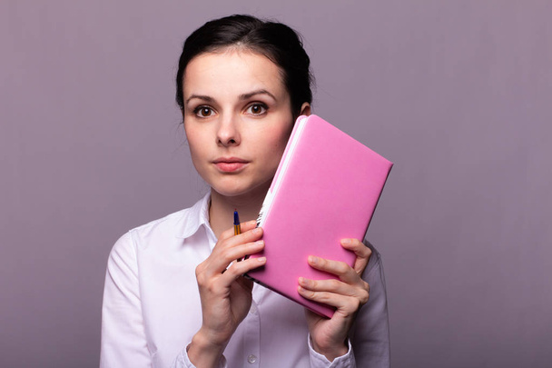 girl in a white shirt holds a pink notebook in her hands - Φωτογραφία, εικόνα