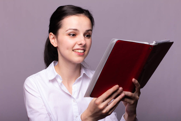 girl in a white shirt holds a red notebook in her hand - Фото, изображение