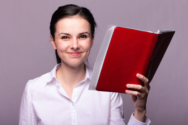 niña con una camisa blanca sostiene un cuaderno rojo en su mano
 - Foto, Imagen