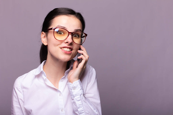 beautiful girl in a white shirt and glasses for vision communicates on the phone - Фото, изображение