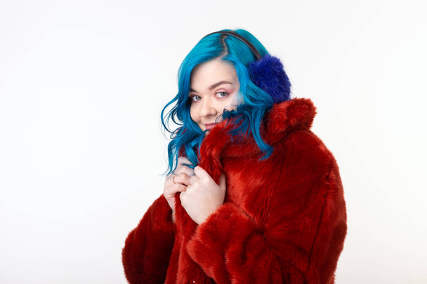 Lidé, ochrana zvířat a módní koncepce-krásná dívka s modrými vlasy oblečenou v červeném teplém kabátku v umělé kožešině a náušníky - Fotografie, Obrázek