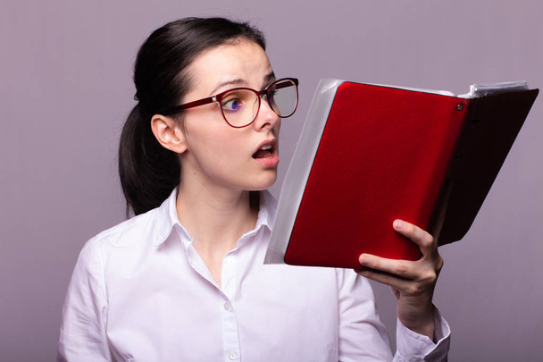 ragazza in camicia bianca e occhiali tiene un notebook rosso in mano
 - Foto, immagini