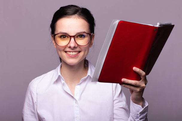 girl in a white shirt and glasses holds a red notebook in her hand - Fotó, kép