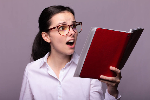 niña con una camisa blanca y gafas lleva un cuaderno rojo en la mano
 - Foto, Imagen