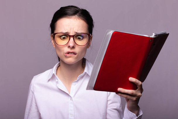 girl in a white shirt and glasses holds a red notebook in her hand - Foto, Bild