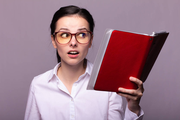 girl in a white shirt and glasses holds a red notebook in her hand - Fotó, kép