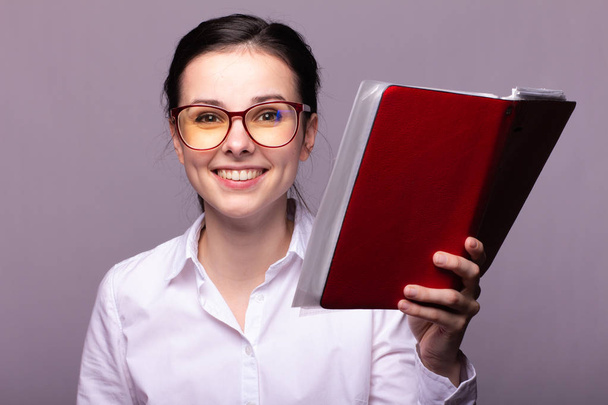 girl in a white shirt and glasses holds a red notebook in her hand - Foto, imagen