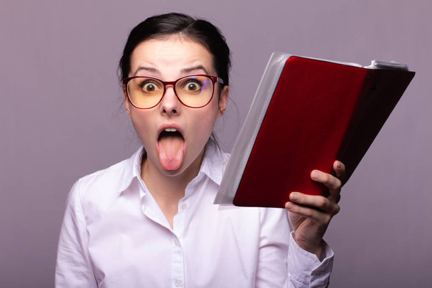 girl in a white shirt and glasses holds a red notebook in her hand - Foto, Imagen