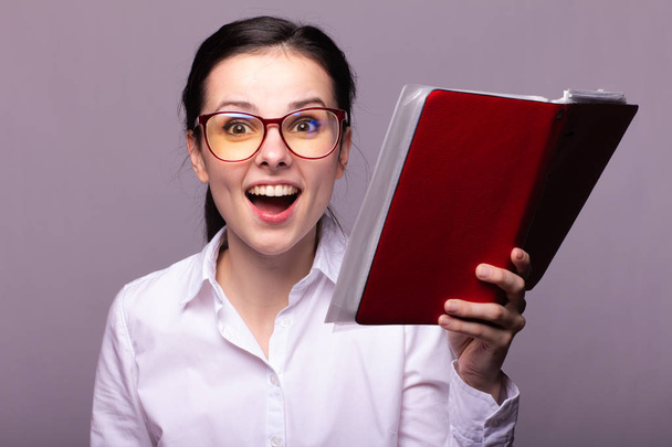 girl in a white shirt and glasses holds a red notebook in her hand - 写真・画像