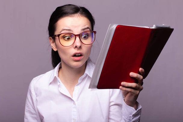 girl in a white shirt and glasses holds a red notebook in her hand - Foto, Imagem