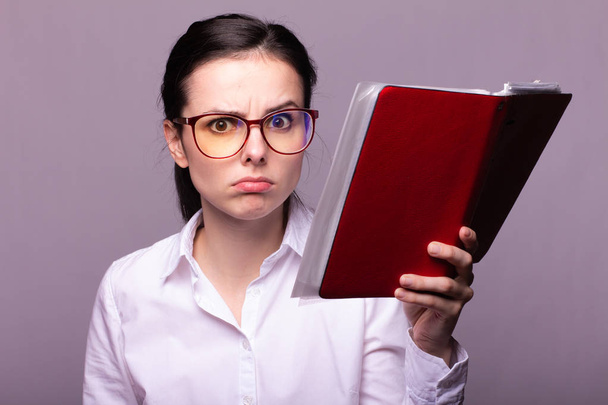 girl in a white shirt and glasses holds a red notebook in her hand - Foto, Bild