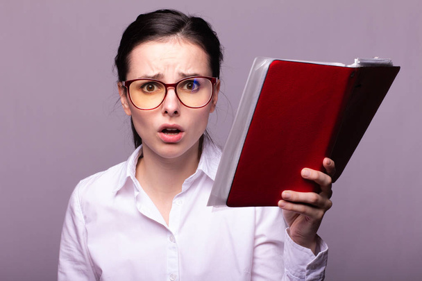 girl in a white shirt and glasses holds a red notebook in her hand - Foto, afbeelding