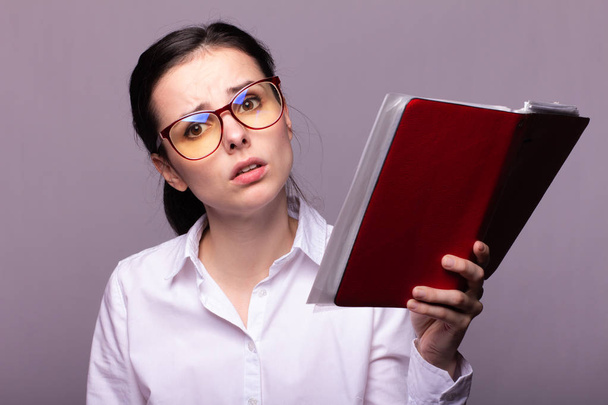 girl in a white shirt and glasses holds a red notebook in her hand - 写真・画像