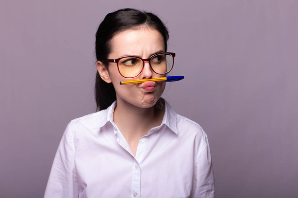 girl in a white shirt and glasses holds a pen with her mouth - Fotoğraf, Görsel