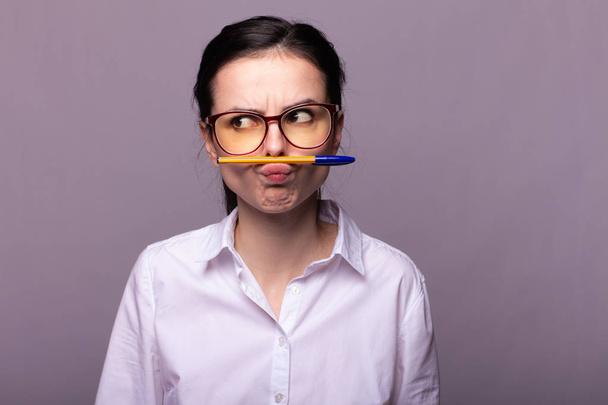 girl in a white shirt and glasses holds a pen with her mouth - Foto, Bild