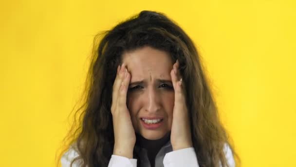 Beautiful girl is suffering from a migraine standing on a yellow background, slow motion - Footage, Video