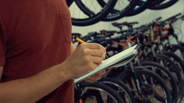 theme of small business selling bicycles. Young Caucasian male brunette small business owner, store manager uses notepad and pen makes notes, checklist at bicycle store - Photo, Image