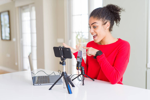 Молоді афро-американської жінки роблять відеодзвінка за допомогою смартфона камера і мікрофон вражений і посміхаючись до камери під час подання з рук і вказуючи пальцем. - Фото, зображення