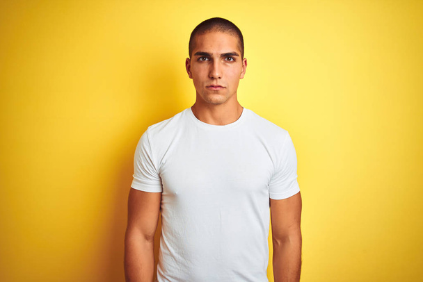 Jeune homme caucasien portant un t-shirt blanc décontracté sur fond jaune isolé sceptique et nerveux, fronçant les sourcils contrariés en raison de problèmes. Personne négative
. - Photo, image