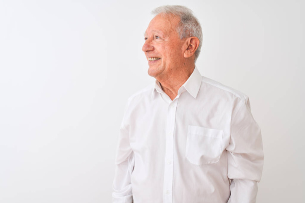 ●白い背景に立つエレガントなシャツを着た先輩の灰色の男が、笑顔で横を向き、自然な表情。自信を持って笑う. - 写真・画像