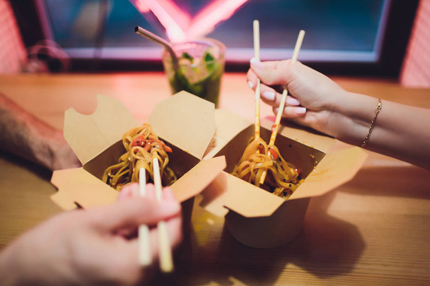 Concept of street food. Chinese Japanese noodles with chicken and vegetables in disposable paper utensils. Copy space, selective focus. on the background of a neon lamp in the shape of a heart - Photo, image