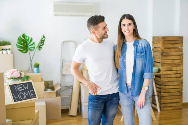 Belo jovem casal se mudando para uma nova casa, sorrindo felizes arround caixas de papelão
 - Foto, Imagem