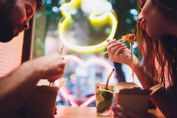 Concept of street food. Chinese Japanese noodles with chicken and vegetables in disposable paper utensils. Copy space, selective focus. on the background of a neon lamp in the shape of a heart. - Foto, Imagem