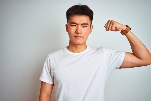 Nuori aasialainen kiinalainen mies yllään t-paita seisoo yli eristetty valkoinen tausta Vahva henkilö osoittaa käsivarren lihas, luottavainen ja ylpeä vallasta
 - Valokuva, kuva