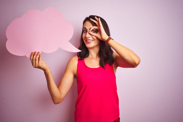 Beautiful woman holding speech bubble over pink isolated background with happy face smiling doing ok sign with hand on eye looking through fingers - Photo, Image