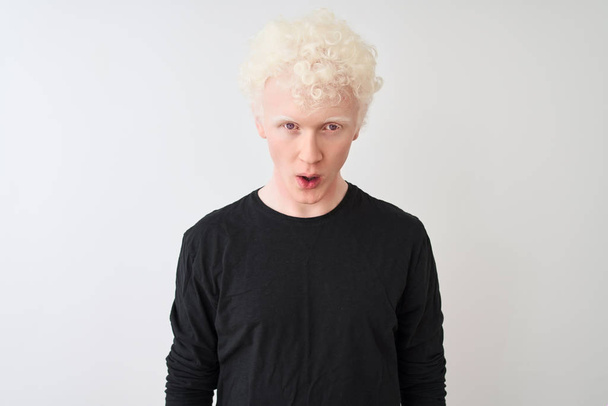 Nuori albiino blondi mies yllään musta t-paita seisoo yli eristetty valkoinen tausta peloissaan ja järkyttynyt yllätys ilme, pelko ja innoissaan kasvot
. - Valokuva, kuva