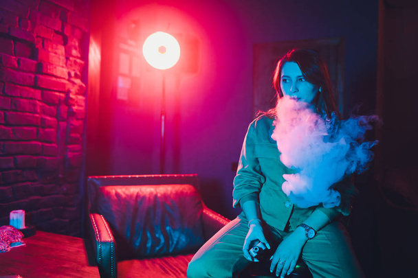 woman smokes a e-cigarette lying on the bed in the room. Smokers concept Vaping. - 写真・画像