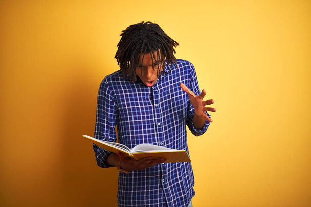 Afro Américain étudiant homme avec dreadlocks lecture livre sur fond jaune isolé très heureux et excité, expression gagnante célébrant la victoire en criant avec un grand sourire et les mains levées
 - Photo, image