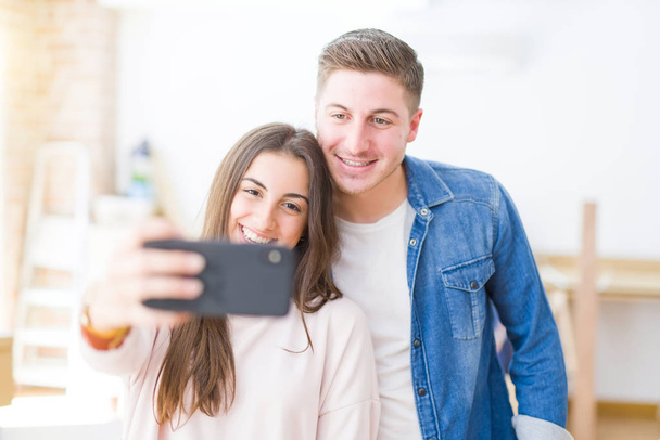 Hermosa pareja joven sonriendo feliz de tomar una foto selfie con el teléfono inteligente, muy emocionado de mudarse a un nuevo hogar
 - Foto, imagen