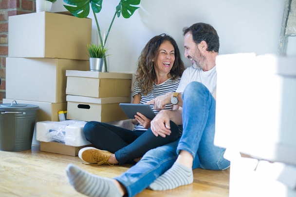 Orta yaş üst düzey romantik çift aşk etrafında kutuları ile daire katında oturan ve Touchpad tablet kullanarak yeni bir eve hareket için mutlu gülümseyen - Fotoğraf, Görsel