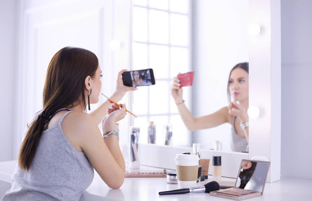 Beauty blogger filming makeup tutorial with smartphone in front of mirror - Foto, imagen