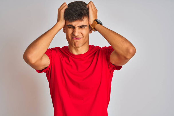 Young indian man wearing red t-shirt standing over isolated white background suffering from headache desperate and stressed because pain and migraine. Hands on head. - Photo, Image