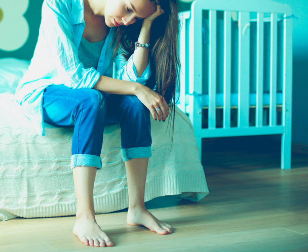 Young tired woman sitting on the bed near childrens cot - 写真・画像