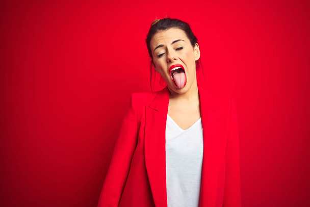 Young beautiful business woman standing over red isolated background sticking tongue out happy with funny expression. Emotion concept. - Fotó, kép