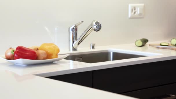 Kitchen countertop made of the granite slab. Counter is made in modern white color with chrome sink and faucet. Kitchen cabinets are made of black flat panels. - Footage, Video