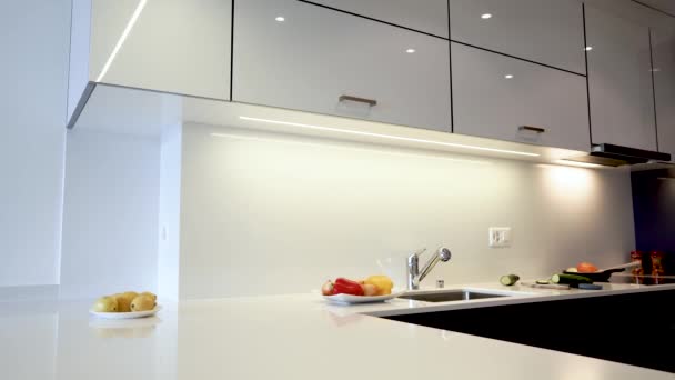 Modern ev iç tasarım mutfak tezgahı üst mutfak dolapları. Dolap kapıları beyaz düz ahşap tahtalardan, tezgahlar ise doğal granit veya mermerden yapılmıştır.. - Video, Çekim
