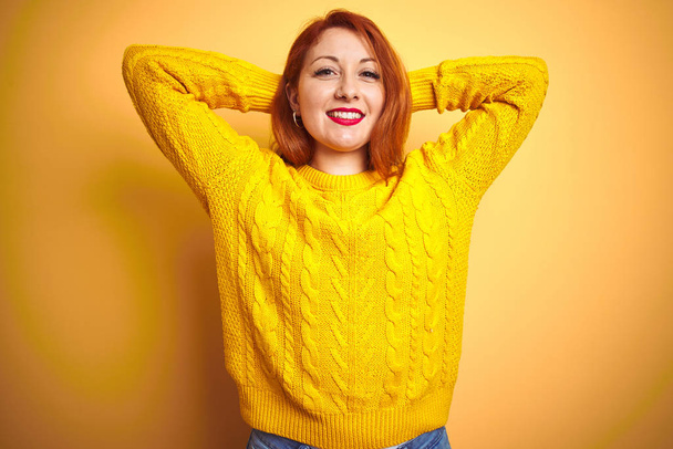 Bella donna rossa che indossa maglione invernale in piedi sopra isolato sfondo giallo rilassante e stretching, braccia e mani dietro la testa e il collo sorridente felice
 - Foto, immagini