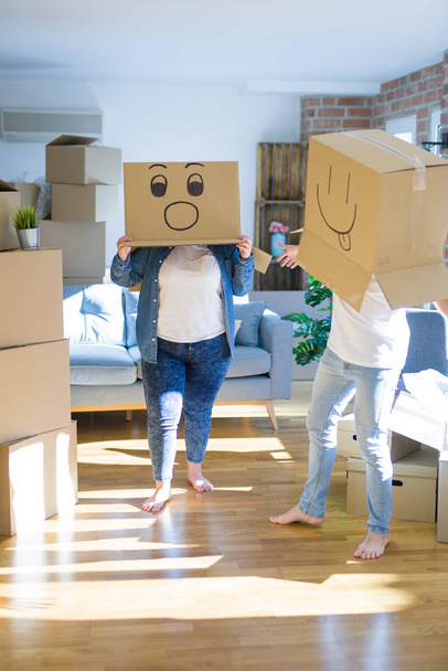 Pareja loca con cajas de cartón con caras divertidas de emoji sobre la cabeza, divirtiéndose en una casa nueva
 - Foto, Imagen
