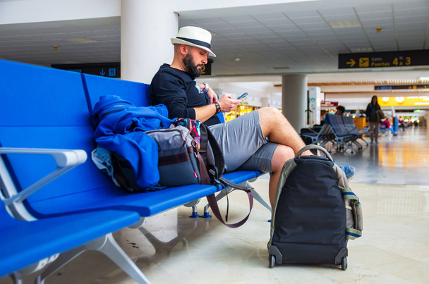 空港で荷物を待っている帽子をかぶった若者 - 写真・画像