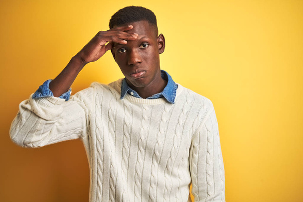Hombre afroamericano vistiendo camisa de mezclilla y suéter blanco sobre fondo amarillo aislado preocupado y estresado por un problema con la mano en la frente, nervioso y ansioso por la crisis
 - Foto, Imagen