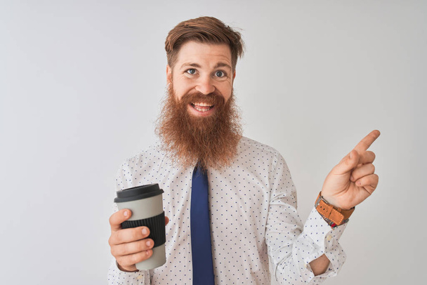 Nuori punapää irlantilainen mies juo ottaa pois kahvia seisoo eristetty valkoinen tausta erittäin onnellinen osoittaa käsin ja sormella sivulle
 - Valokuva, kuva