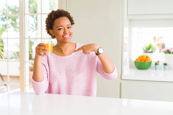 Jovem afro-americana pingando suco de laranja em casa com o rosto surpresa apontando o dedo para si mesmo
 - Foto, Imagem