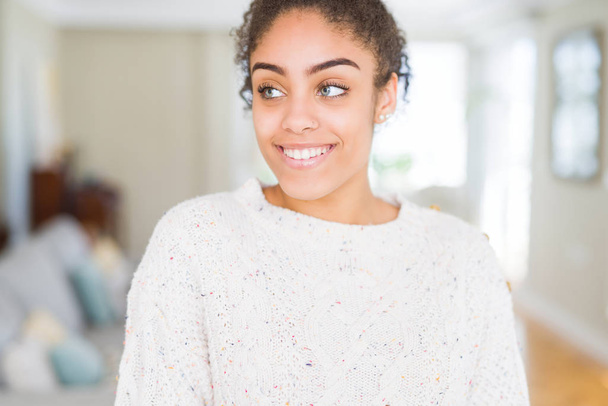 Красивая молодая африканская американка с афроволосами в повседневном свитере улыбается и смотрит в сторону, думая:
. - Фото, изображение