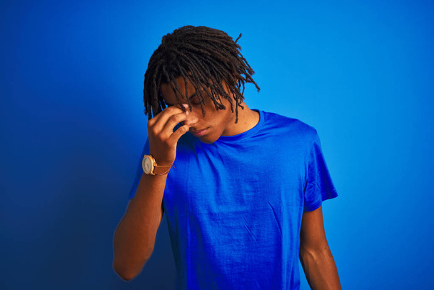 Homme afro-américain avec dreadlocks portant t-shirt debout sur fond bleu isolé fatigué se frottant le nez et les yeux ressentant fatigue et maux de tête. Concept de stress et de frustration
. - Photo, image