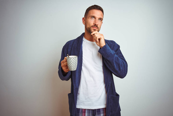 Мужчина в удобной пижаме и халате, пьющий чашку кофе на изолированном фоне, раздраженный и разочарованный, кричащий от злости, сумасшедший и кричащий с поднятой рукой, гнев концепции
 - Фото, изображение